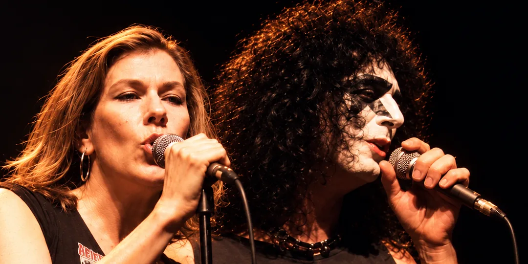Both vocalists from The Ducks side by side at their microphones under amber light